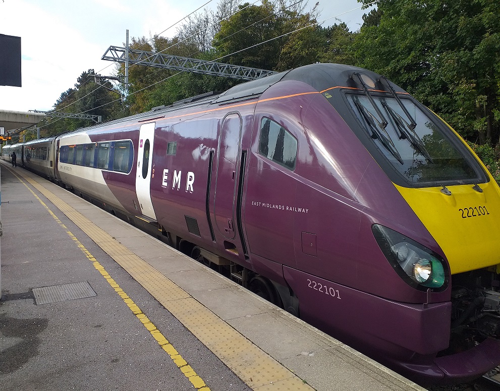 Predominately purple liveried modern train standing at a the platform of Corby station.